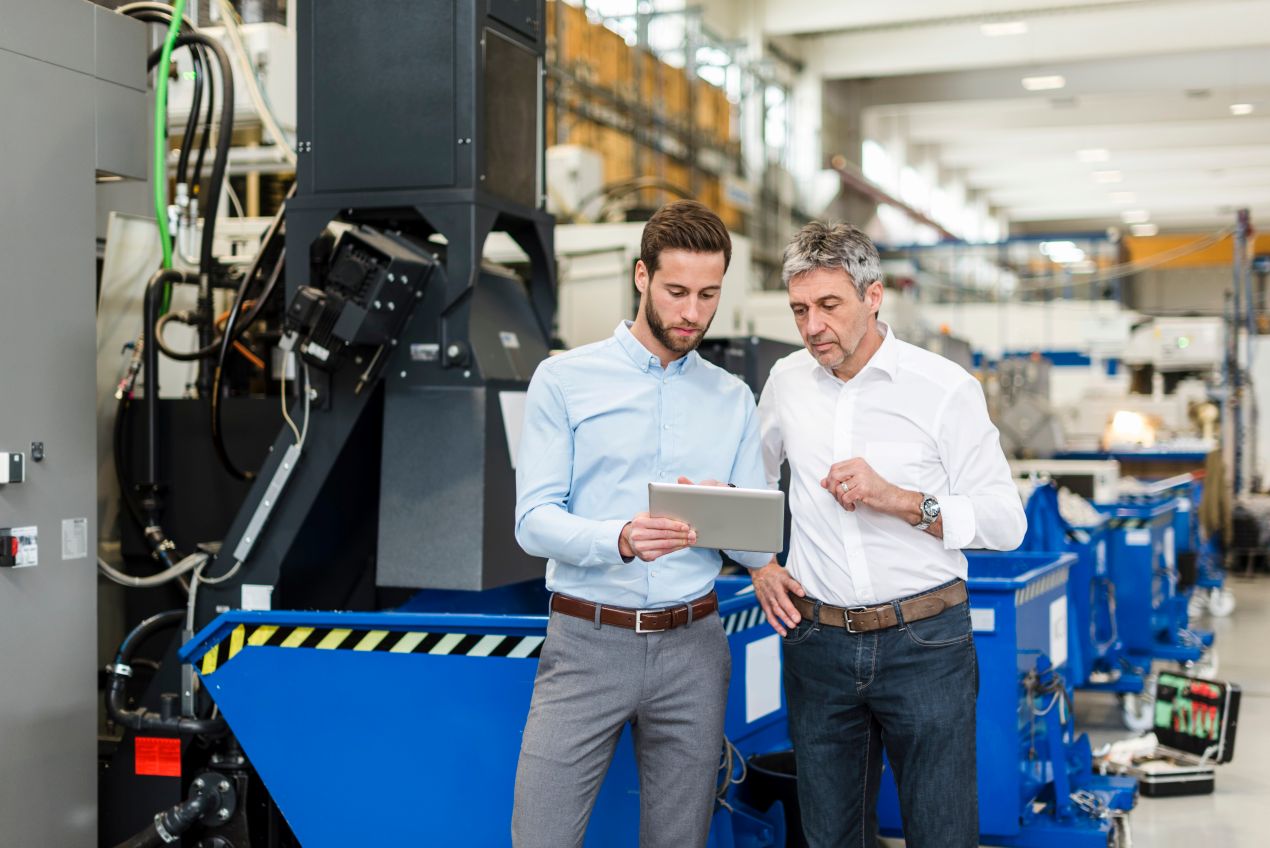 Produktionsleiter und Ingenieur stehen in Werkshalle mit Tablet zur Planung und Umsetzung von Produktionsautomatisierung in der Industrie