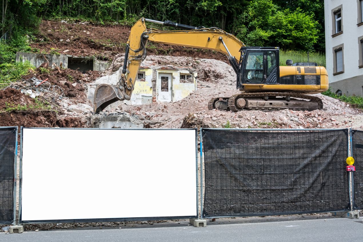 Bauzaunbanner neben Bagger auf Abrissbaustelle mit leerer Fläche zur individuellen Werbegestaltung